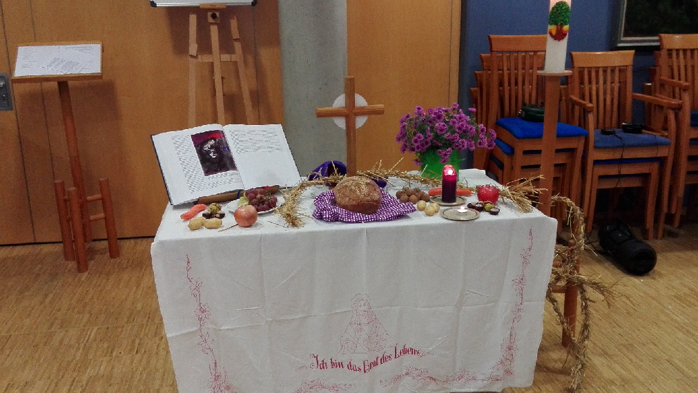 Das Bild zeigt einen Altar mit Holzkreuz in der Mitte, eine Bibel links davon aufgeschlagen, Kerzen und geschmückt mit Brot und verschiedenen Früchten